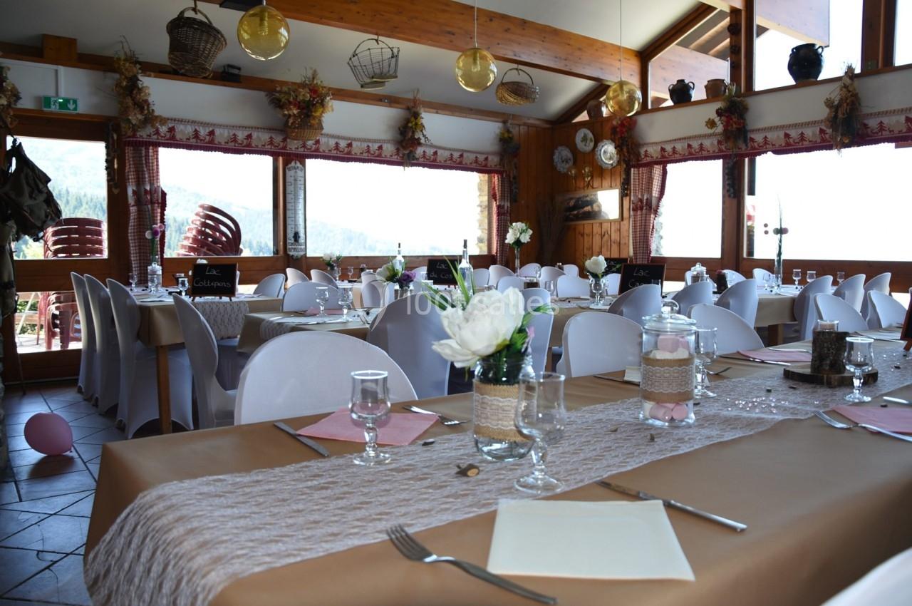 Salle de réception décorée avec des tables dressées, nappes beige, fleurs blanches et grandes fenêtres donnant sur l…