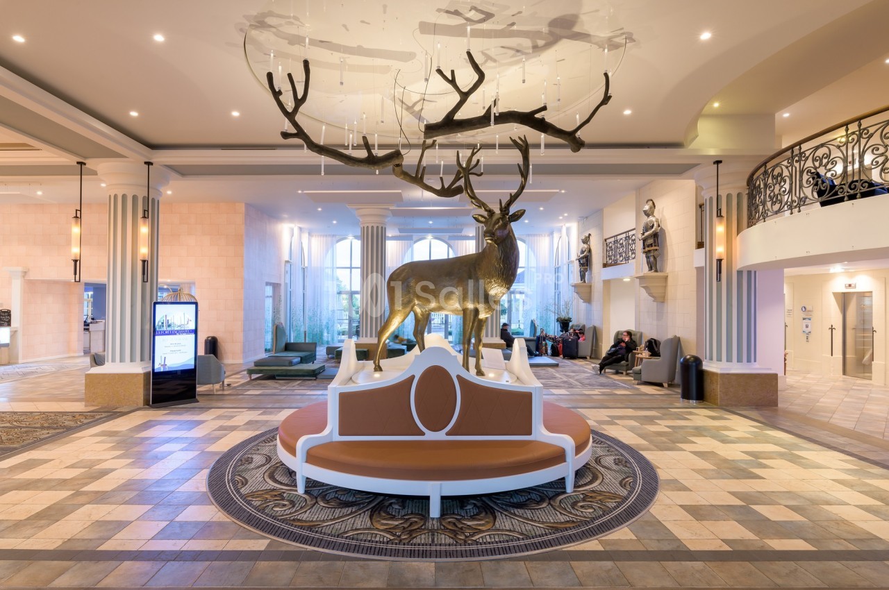 Statue de cerf doré au centre d'un hall spacieux avec banc circulaire, colonnes et éclairage moderne.
