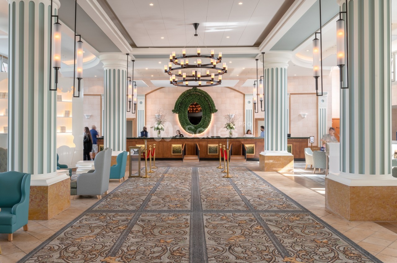 Hall spacieux avec colonnes décoratives, lustre central, comptoir de réception en bois et fauteuils modernes.