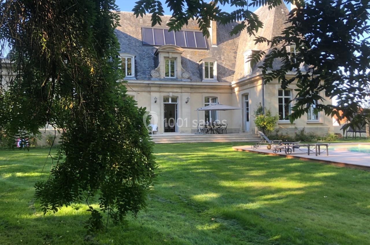 Façade arrière d'une maison en pierre avec toit en ardoise, terrasse aménagée, piscine et jardin verdoyant.