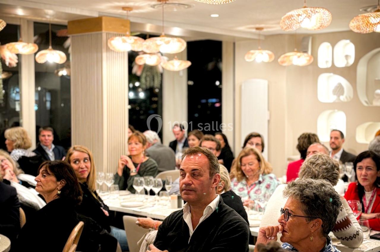Des personnes assises dans un restaurant élégant, participant à un événement ou une réunion, entourées de tables dressées.