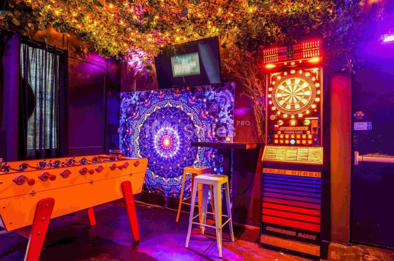 Salle de loisirs avec baby-foot, jeu de fléchettes électronique, décorations lumineuses et mur orné d'un motif coloré.