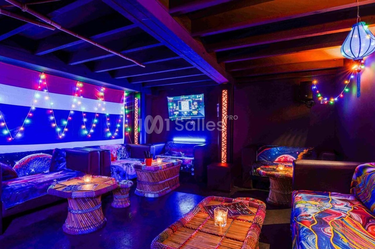 Salle colorée avec canapés, tables en osier, éclairage tamisé et guirlandes lumineuses décoratives.