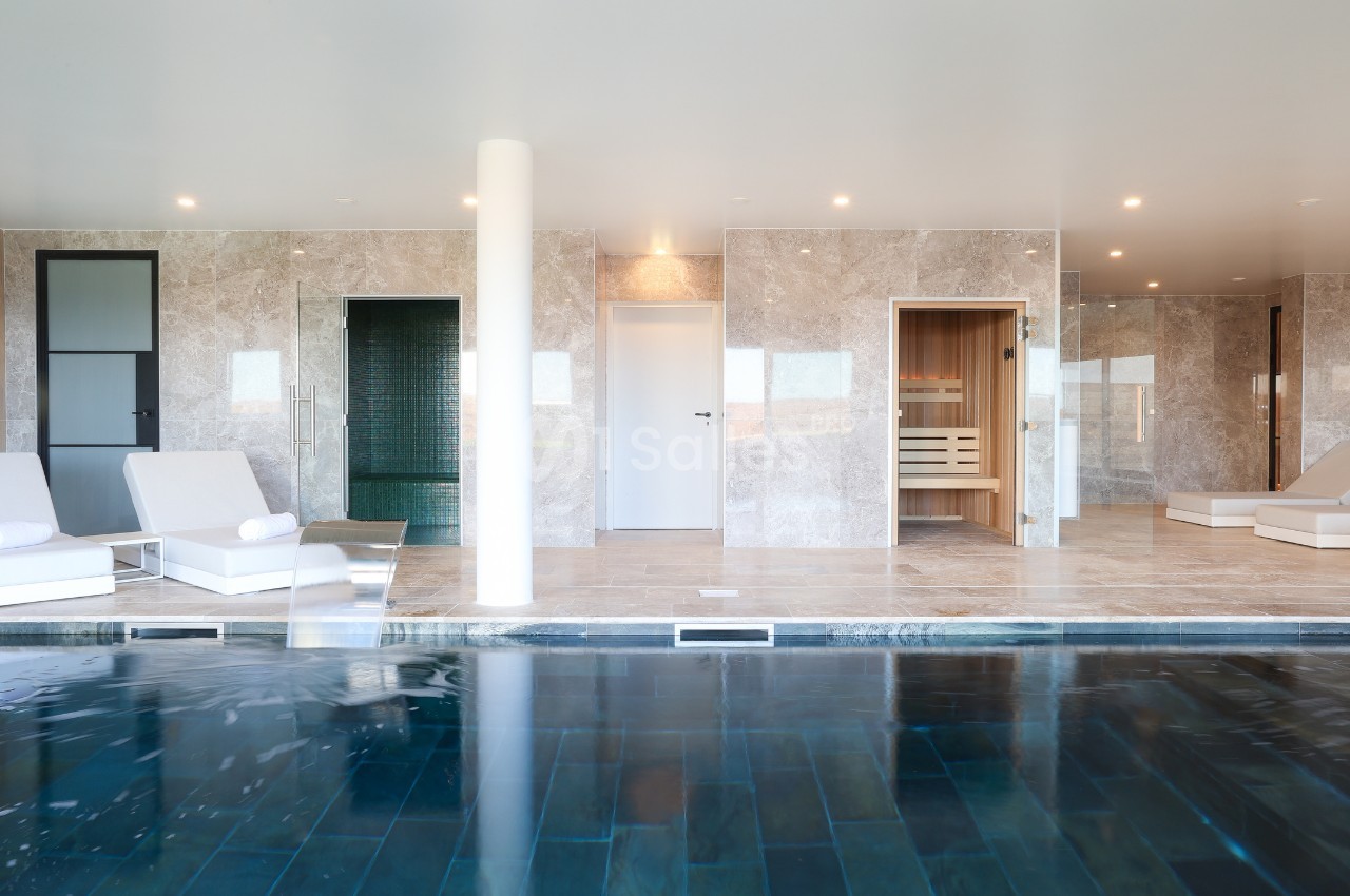 Piscine intérieure avec chaises longues, murs en marbre, sauna et hammam visibles en arrière-plan.