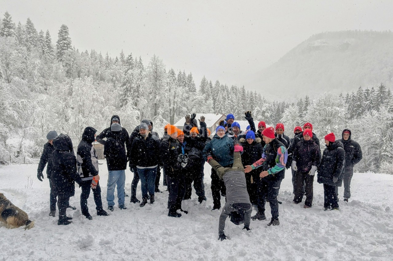 Un groupe de personnes habillées chaudement pose dans un paysage enneigé avec des arbres et des collines en arrière-plan.