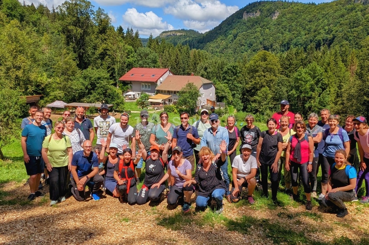 Un groupe de personnes pose en extérieur devant un paysage verdoyant avec des collines et un bâtiment en arrière-plan.
