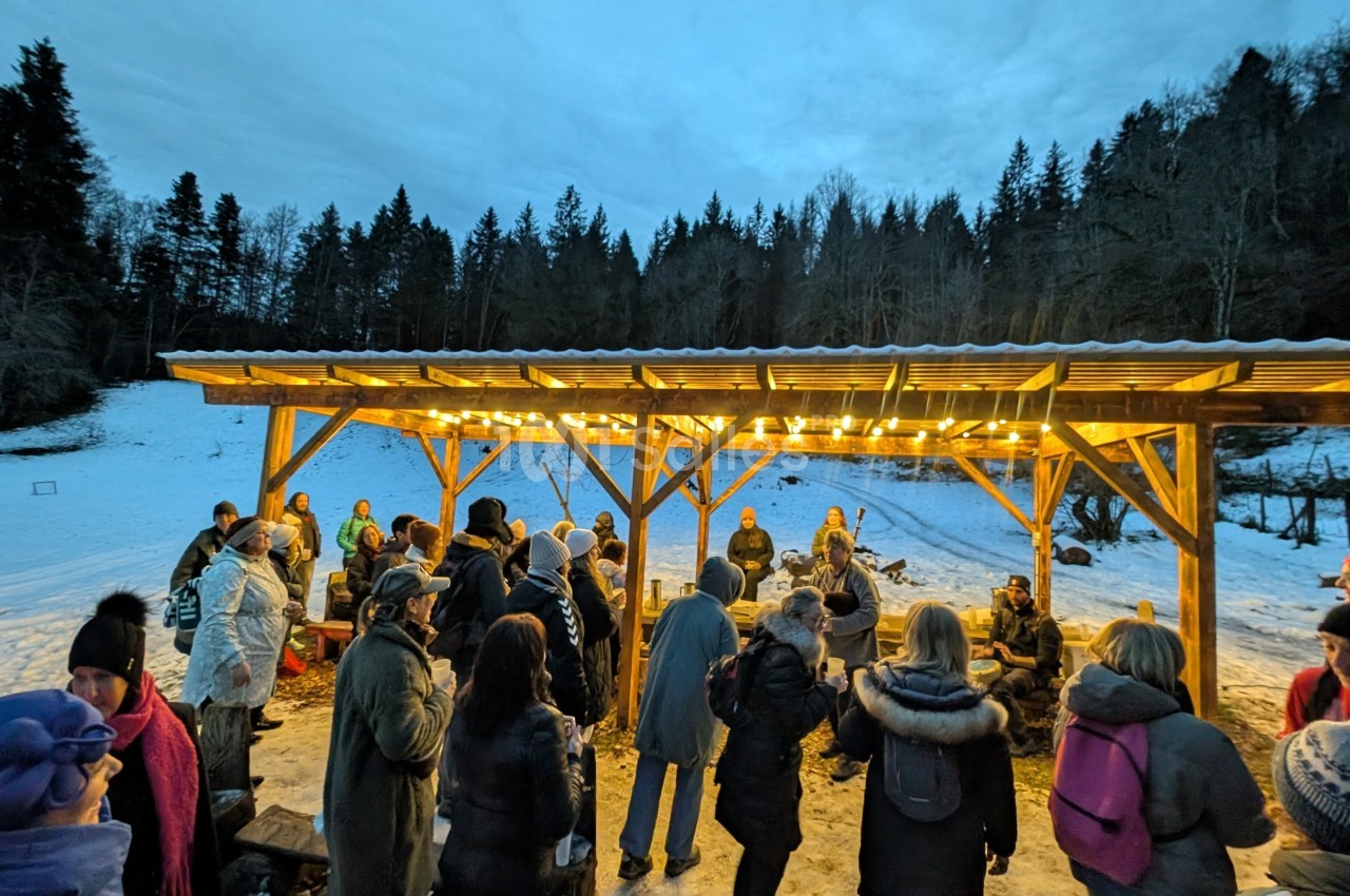 Groupe de personnes rassemblées sous un abri éclairé en bois, entouré de neige et d'arbres en arrière-plan.