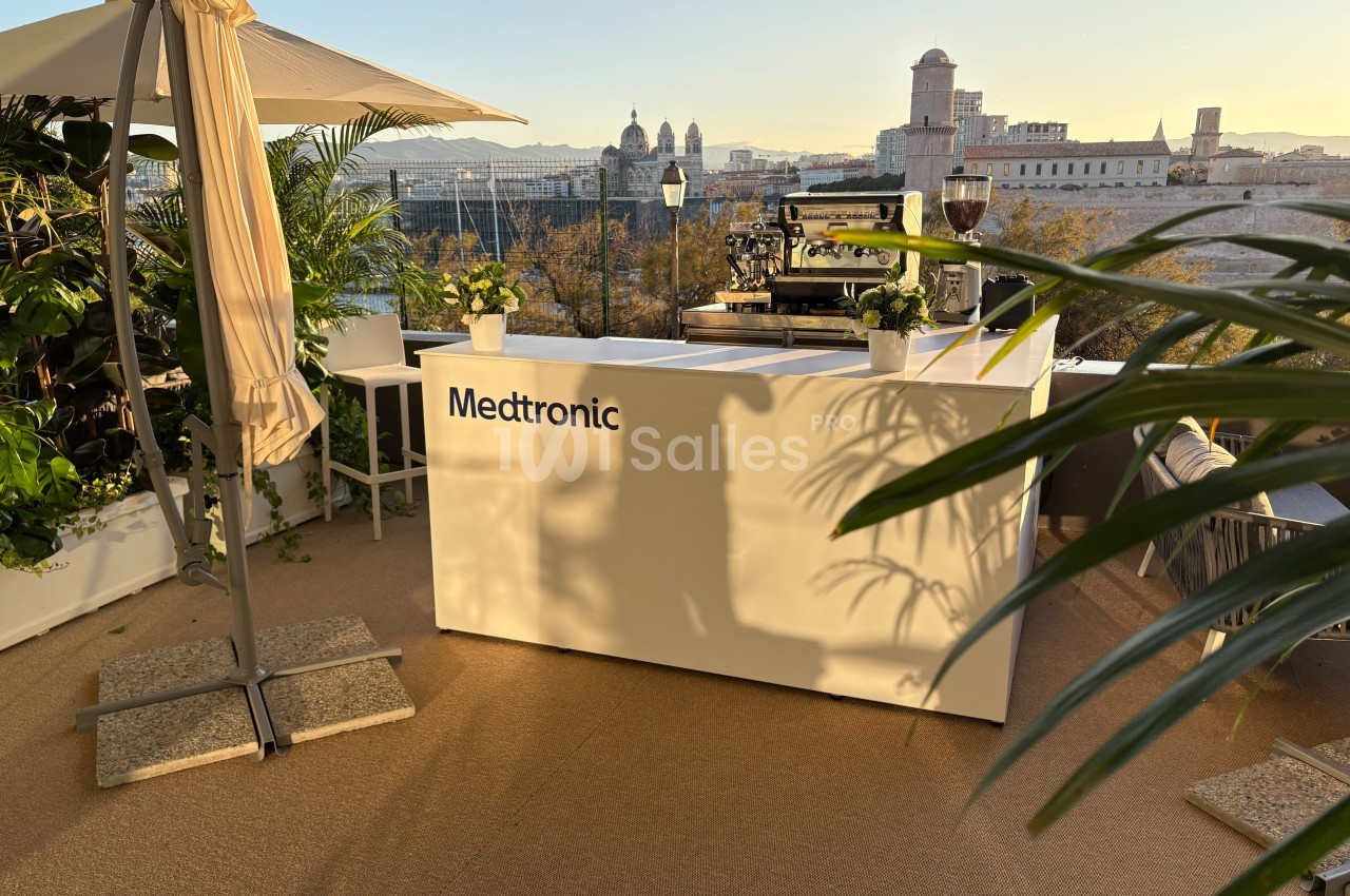 Comptoir blanc avec logo ’Medtronic’ sur une terrasse ensoleillée, entouré de plantes et vue sur des bâtiments historiques.
