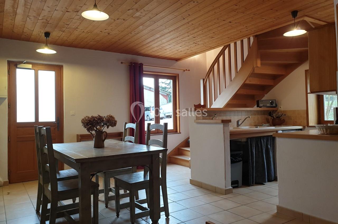 Salle à manger avec table en bois, chaises assorties, escalier en bois, et cuisine ouverte dans un intérieur chaleureux.