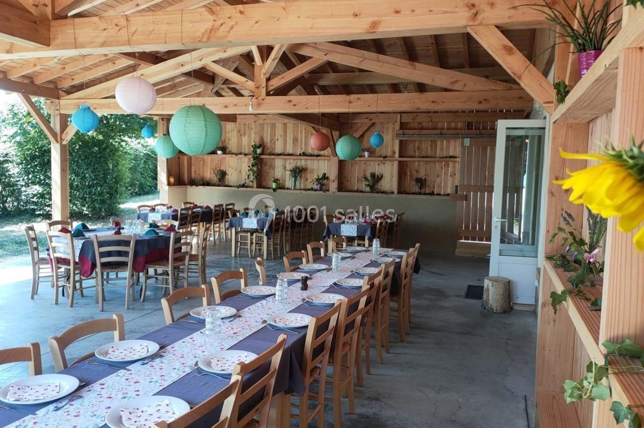 Salle en bois décorée avec des lanternes colorées, tables dressées avec nappes et assiettes pour un repas collectif.