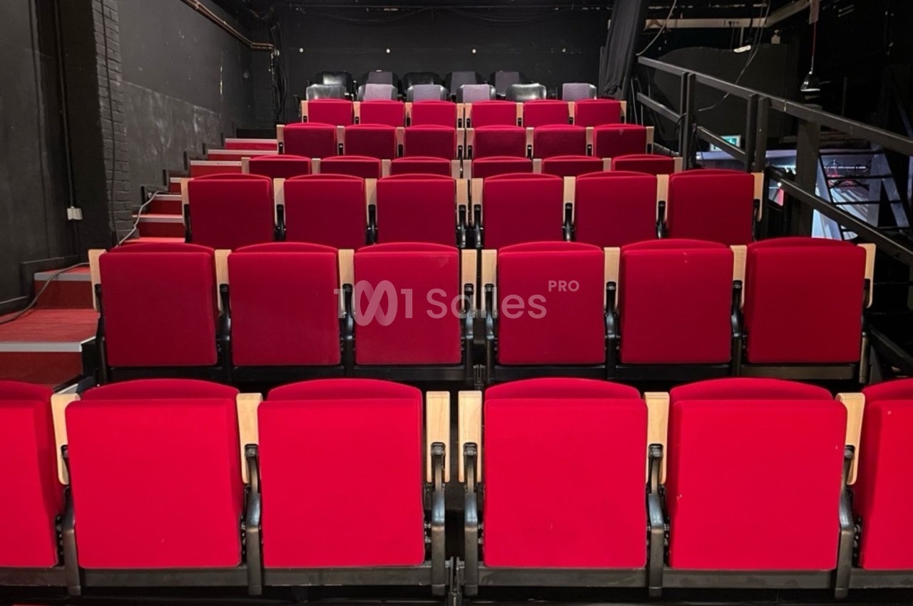 Rangées de fauteuils rouges alignés dans une petite salle de spectacle ou de théâtre.