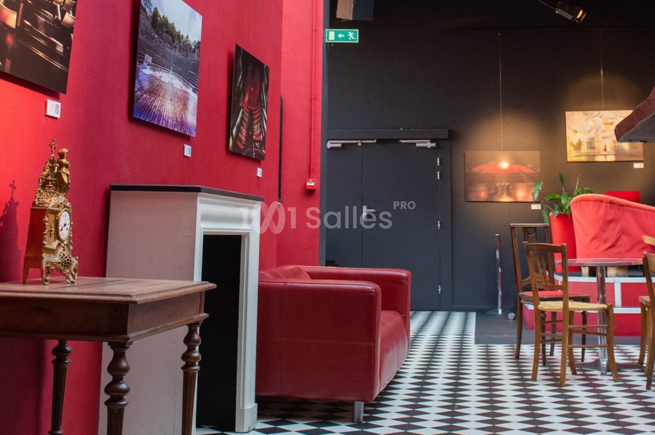 Salon avec murs rouges, sol à carreaux noirs et blancs, mobilier en bois, fauteuils rouges et décorations murales.