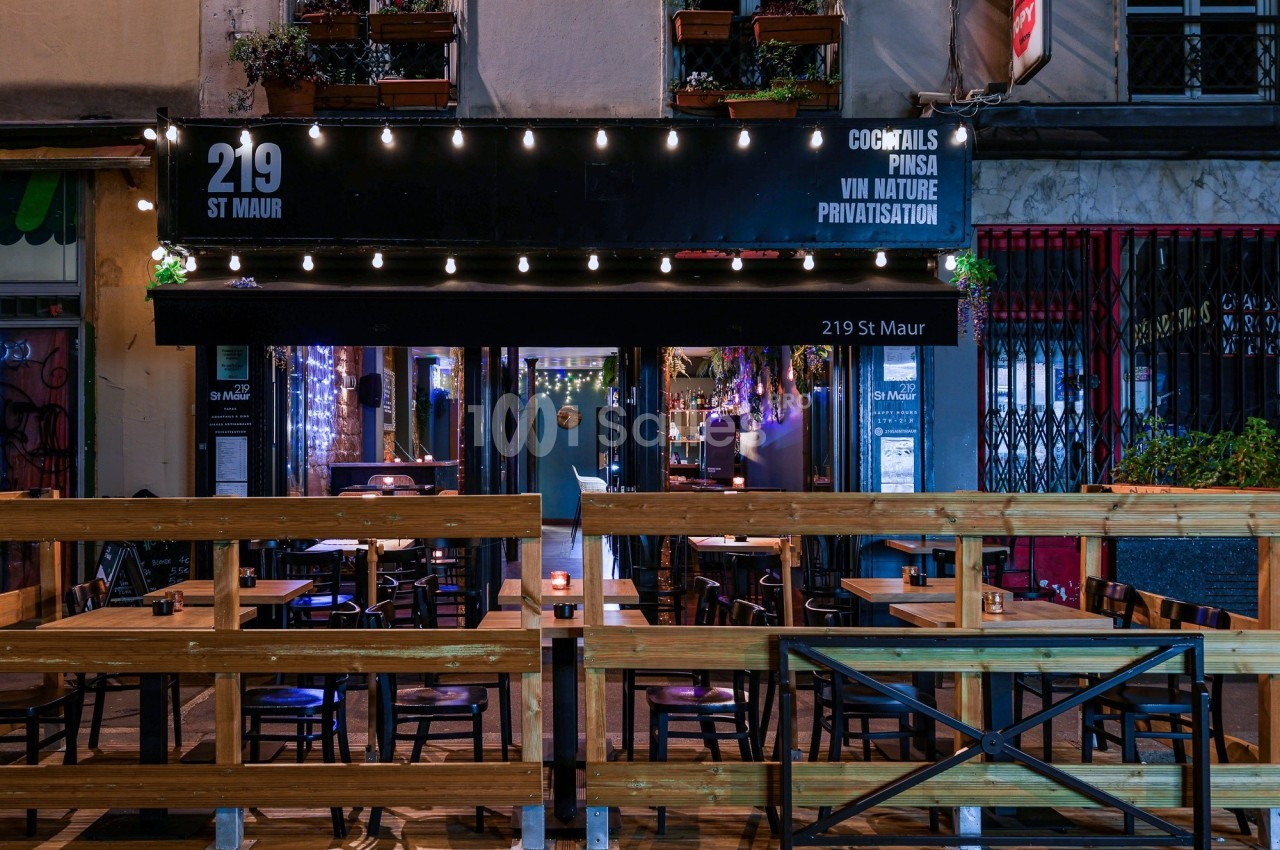 Façade d'un bar-restaurant avec terrasse en bois, éclairage nocturne et enseigne ’219 St Maur’.