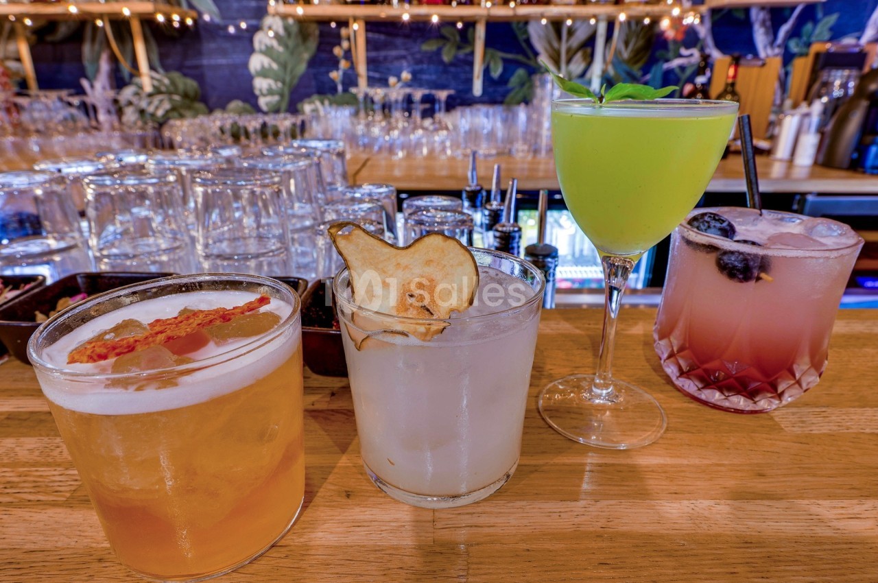 Quatre cocktails variés disposés sur un comptoir en bois, avec des décorations et des verres en arrière-plan.