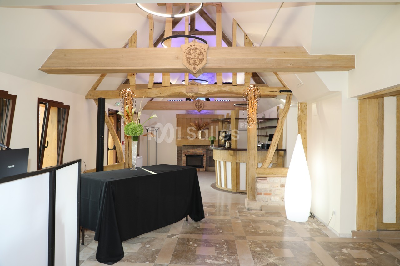 Intérieur d'une salle avec poutres apparentes en bois, comptoir en fond et sol en pierre.
