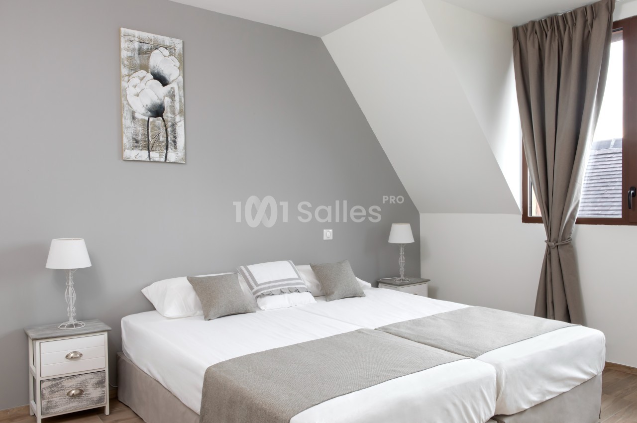 Chambre lumineuse avec un lit double, des murs gris, des rideaux assortis et deux tables de chevet avec lampes.