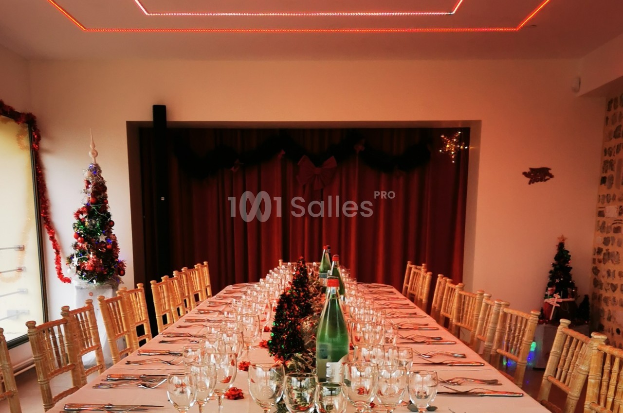 Grande table dressée pour un repas festif, décorée de guirlandes rouges et entourée de chaises en bois.