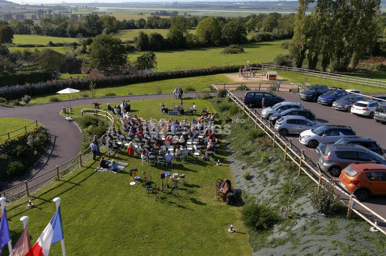 Vue aérienne d'un rassemblement en plein air avec des chaises disposées sur une pelouse, entouré de voitures et de paysages…