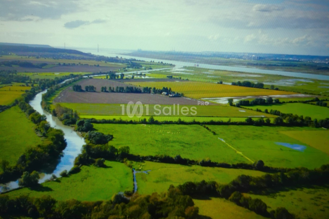 Vue aérienne d'une campagne verdoyante avec des champs, un cours d'eau sinueux et un horizon dégagé.