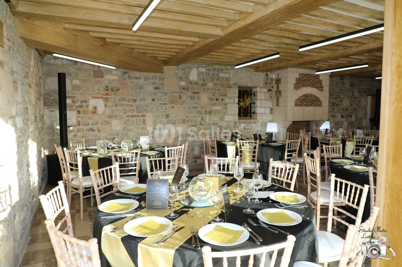 Salle de réception en pierre avec tables dressées, nappes noires et jaunes, et chaises en bois clair.