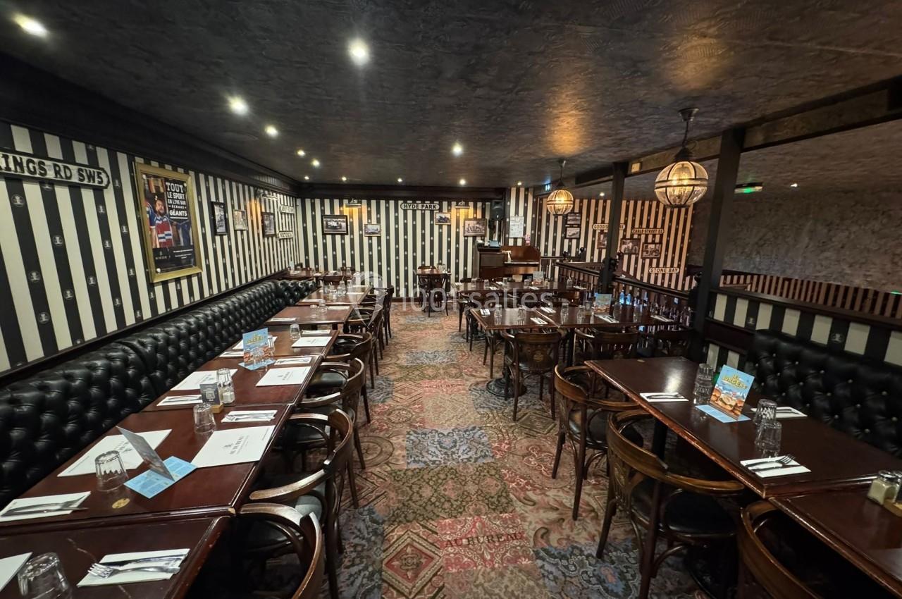 Salle de restaurant avec tables en bois sombre, chaises assorties, banquettes noires et décoration murale rayée.