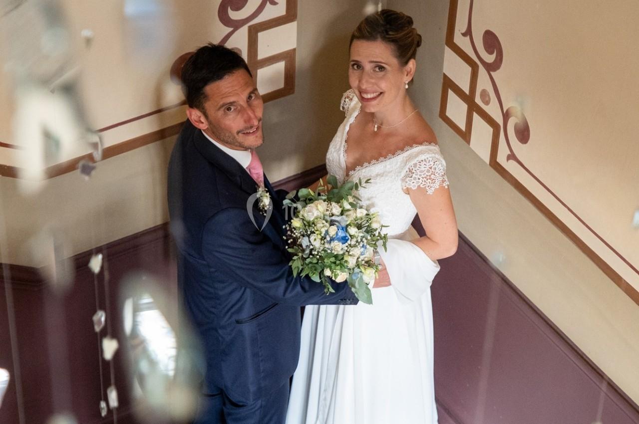 Un couple de mariés souriants pose dans un escalier décoré, tenant un bouquet de fleurs.