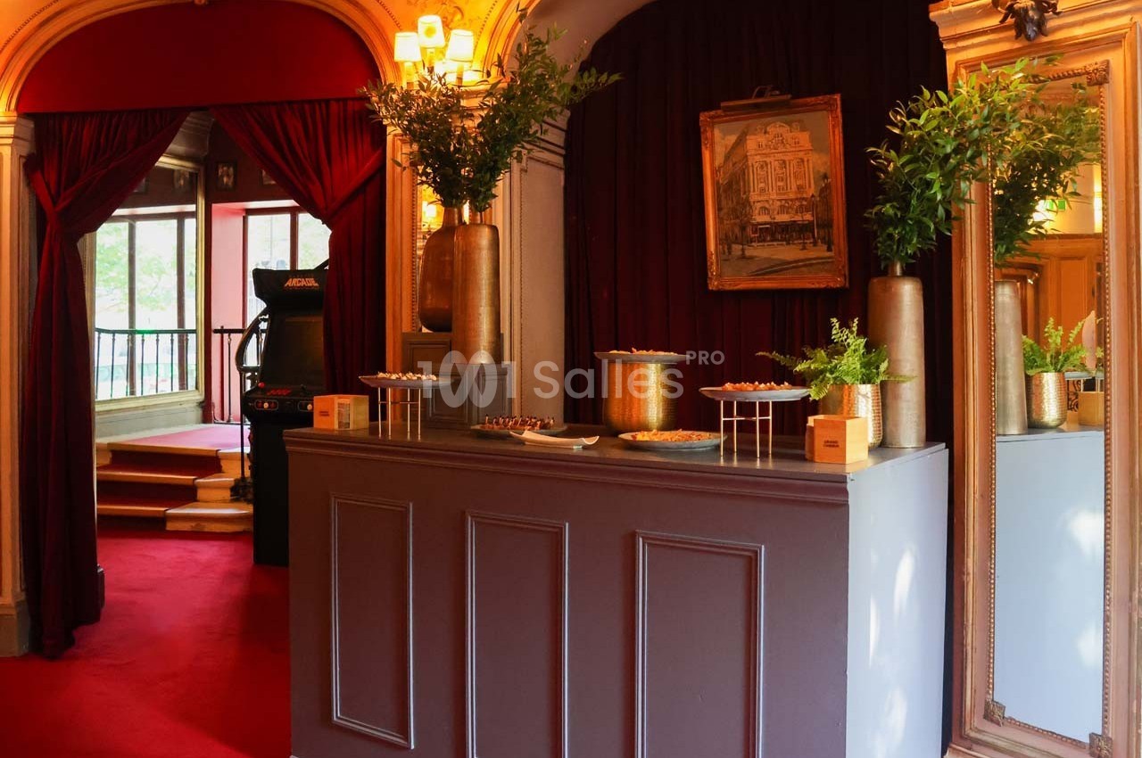 Comptoir décoré avec des plantes, des plateaux et un tableau encadré, dans un intérieur aux tons rouges et dorés.