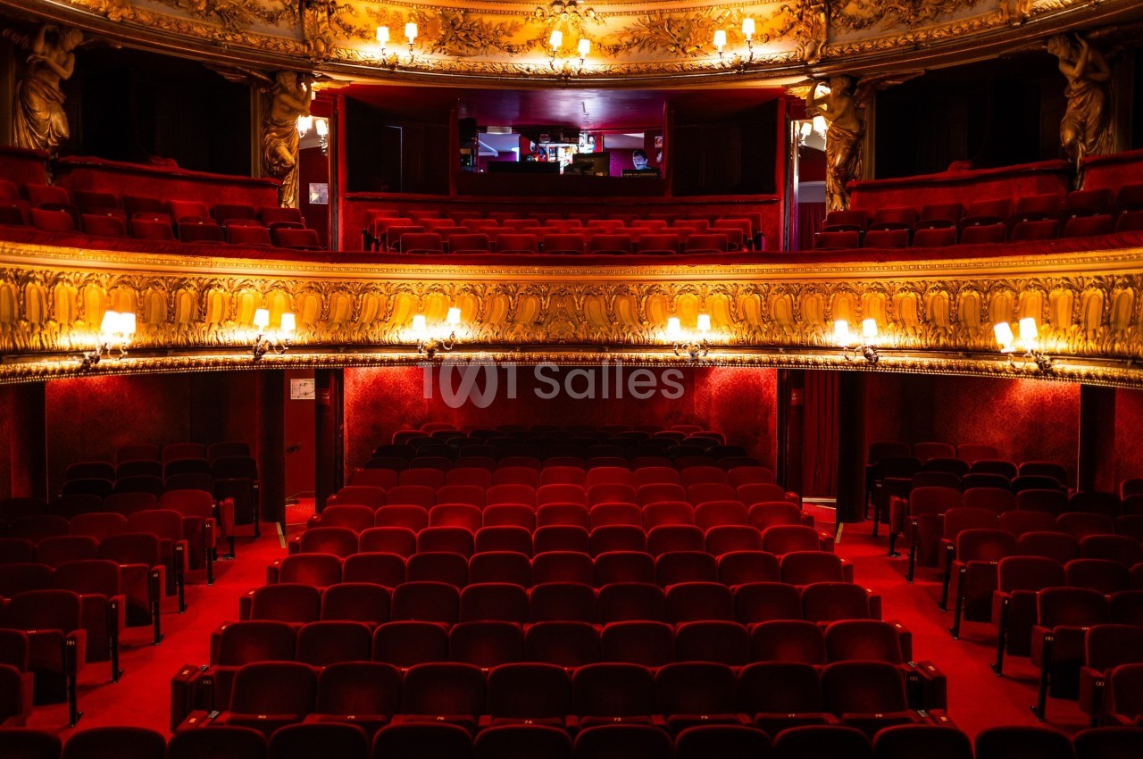 Salle de théâtre vide avec des sièges rouges, balcons ornés et éclairage chaleureux.