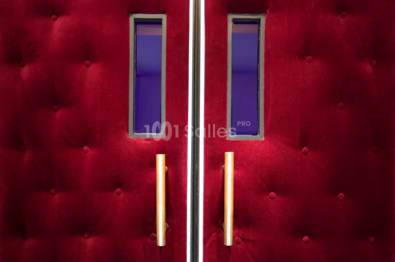 Portes capitonnées rouges avec poignées dorées et petites fenêtres rectangulaires laissant entrevoir une lumière violette.