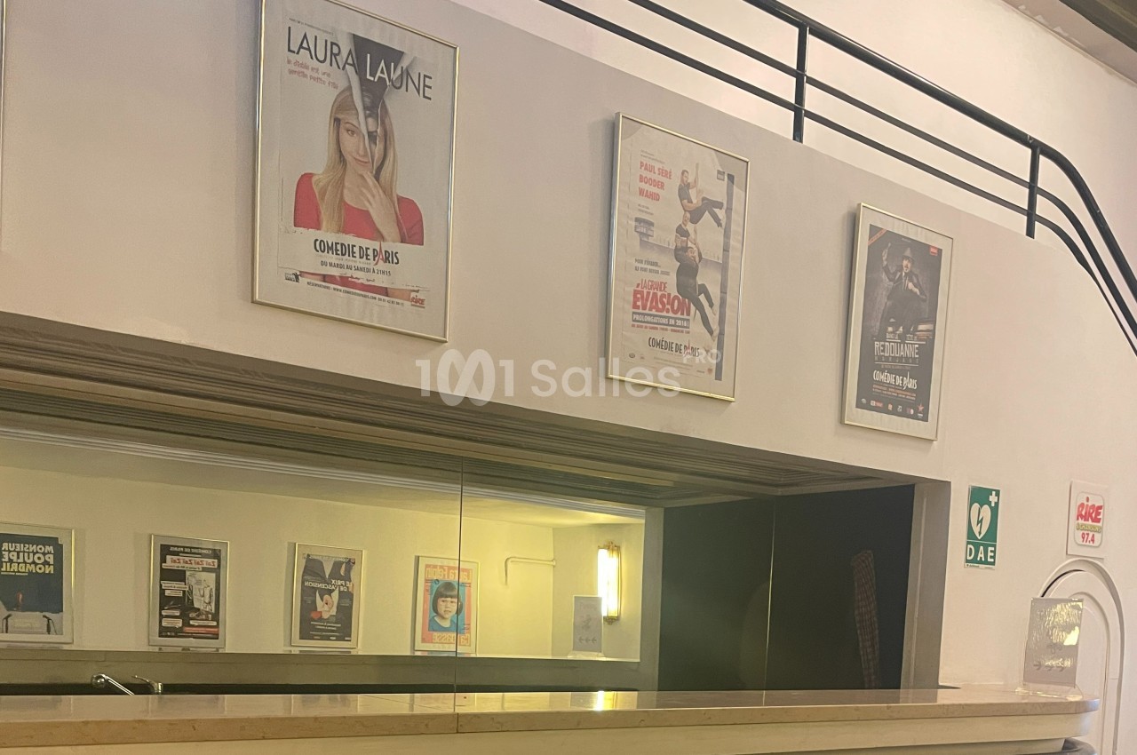 Affiches de spectacles accrochées au mur au-dessus d'un comptoir dans un espace intérieur avec signalétique de sécurité.