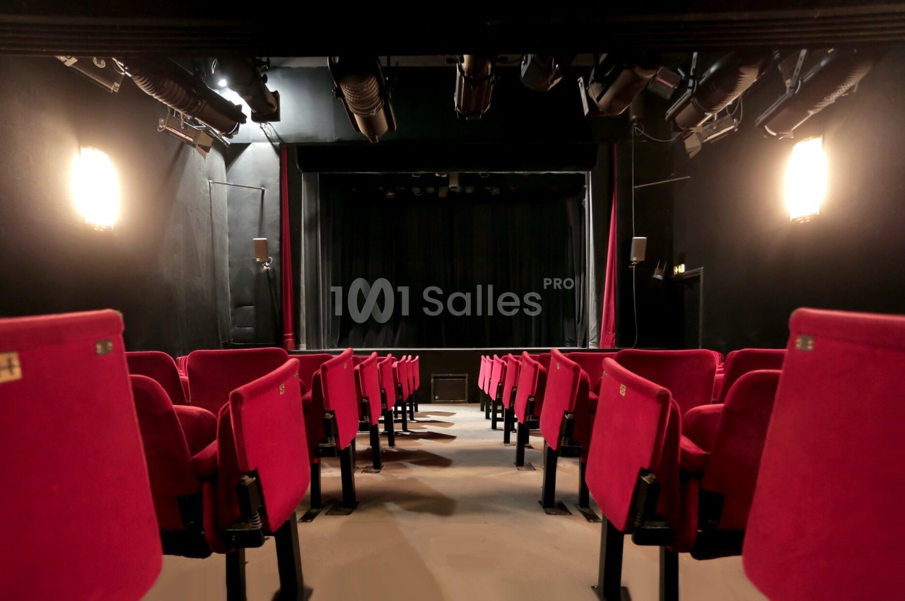 Salle de théâtre vide avec des rangées de sièges rouges et une scène sombre en arrière-plan.