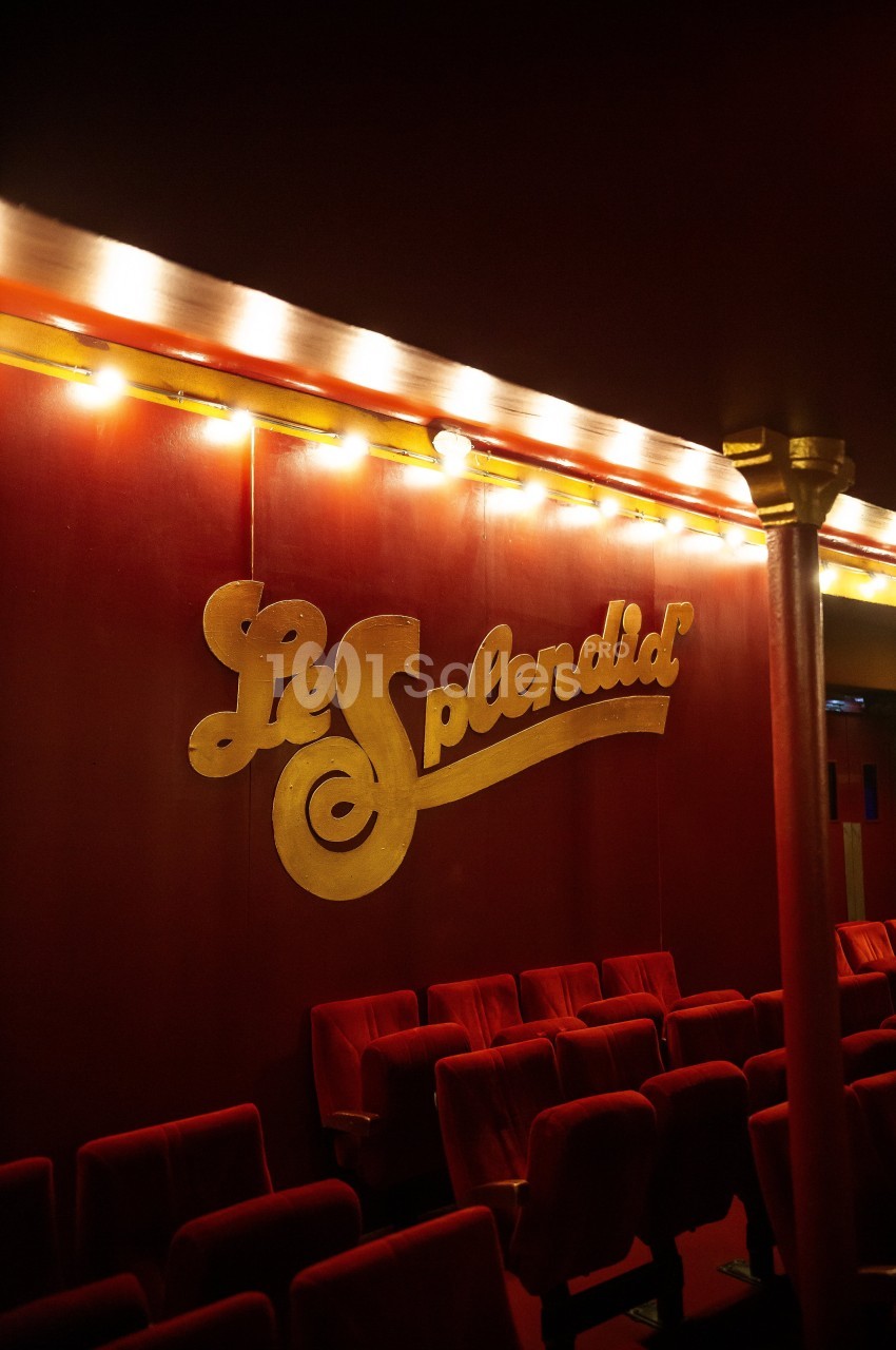 Salle de théâtre avec des rangées de fauteuils rouges et une enseigne murale dorée indiquant ’Le Splendid’.
