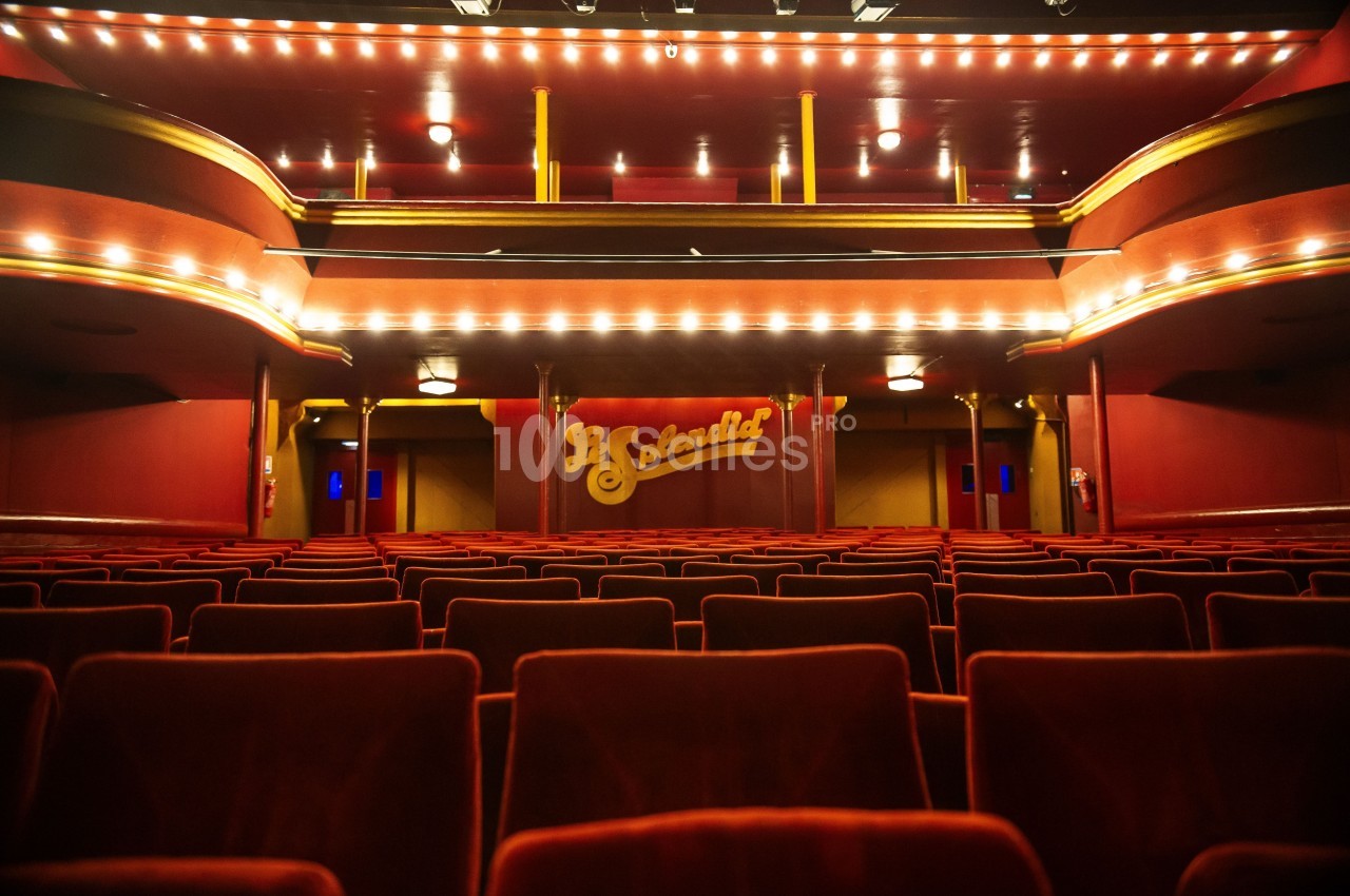 Salle de théâtre vide avec des rangées de fauteuils rouges et une scène ornée du nom ’Le Splendid’.