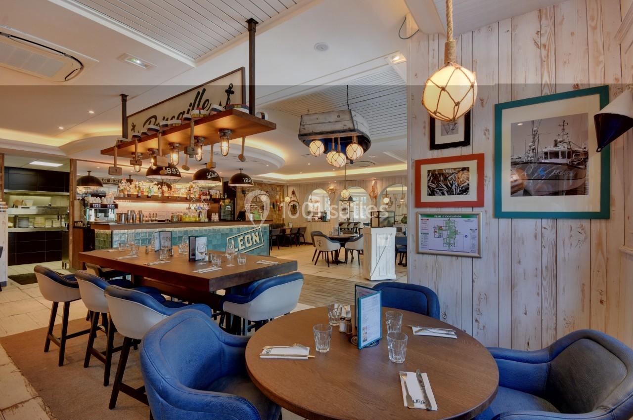 Salle de restaurant lumineuse avec décoration maritime, tables dressées et vue sur le bar en arrière-plan.