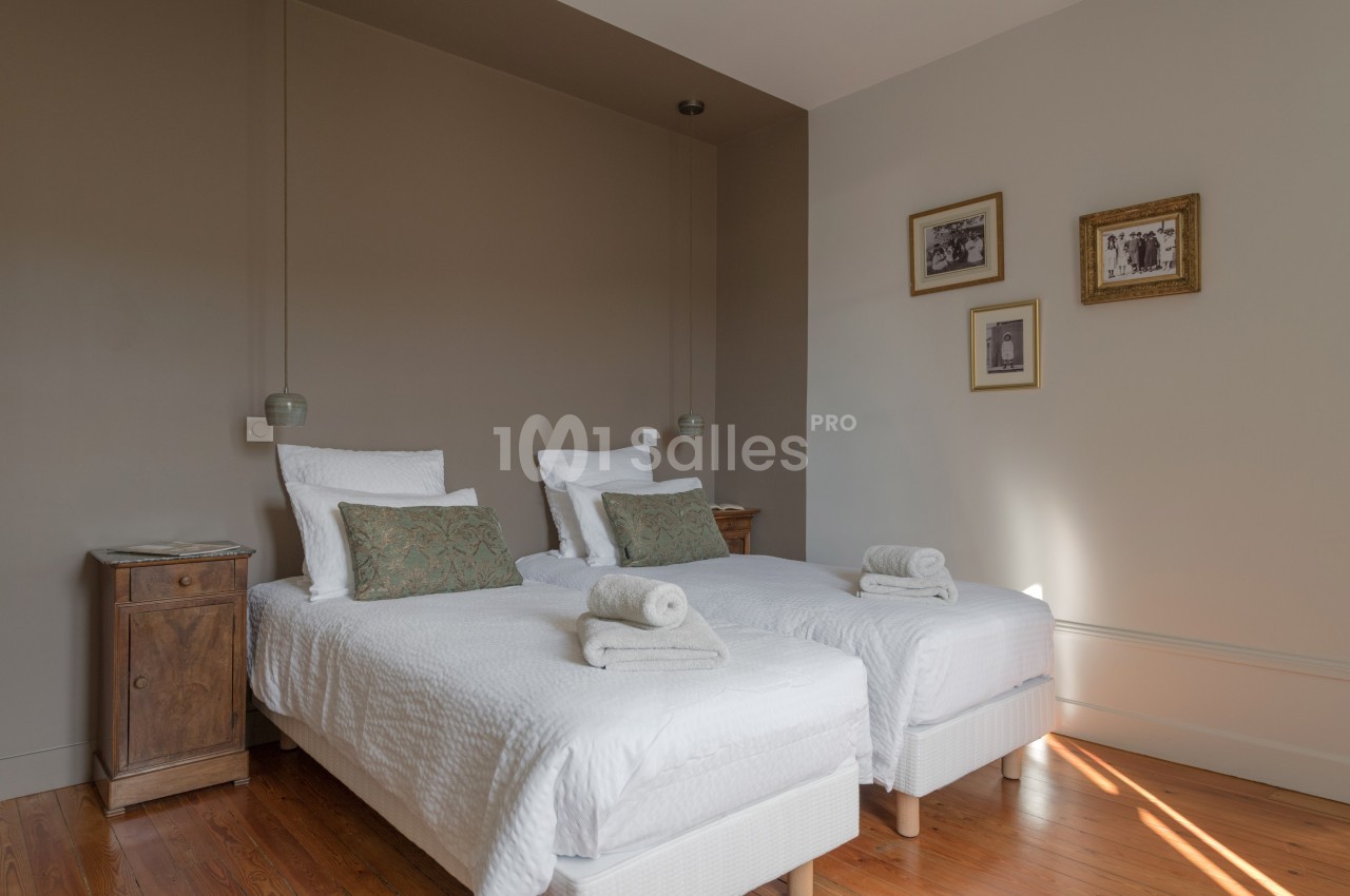 Deux lits simples avec linge blanc, coussins verts et tables de chevet en bois dans une chambre lumineuse.