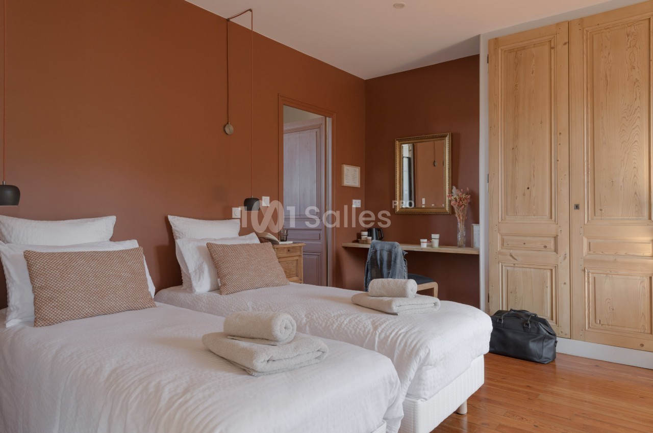 Chambre avec deux lits simples, murs couleur terre cuite, mobilier en bois clair et lumière naturelle.