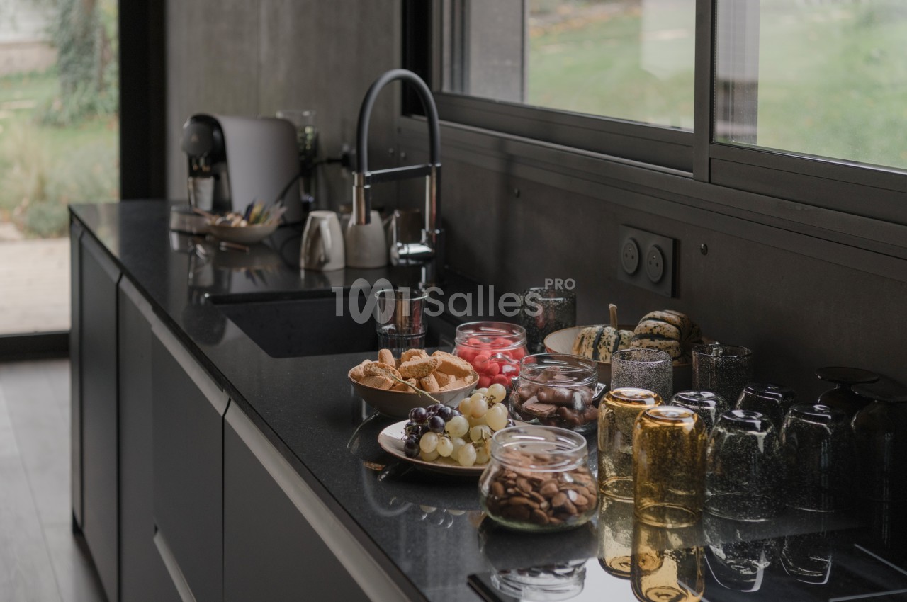 Plan de travail de cuisine moderne avec évier, bocaux de nourriture, fruits et vaisselle près d'une fenêtre.