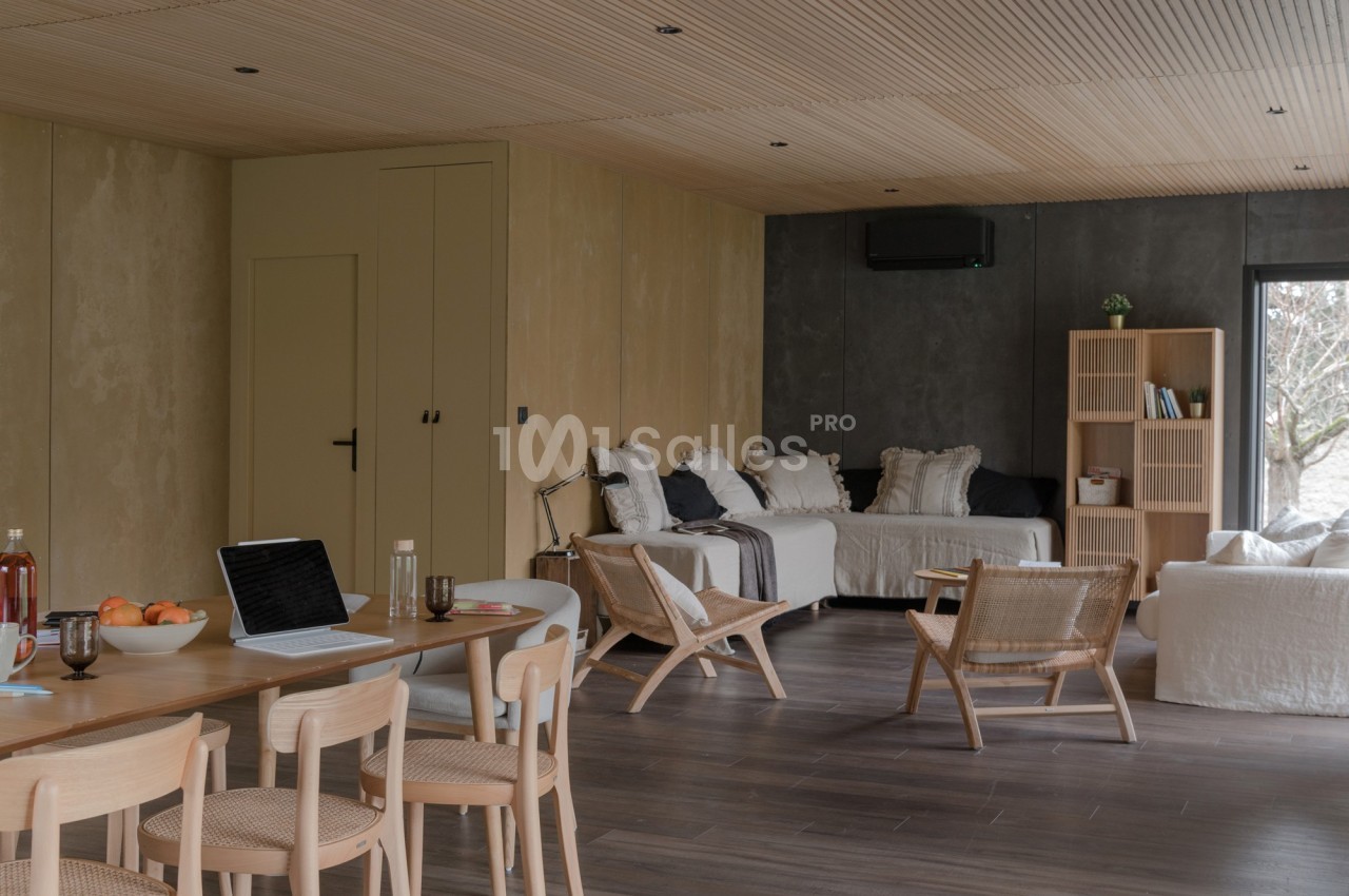 Salle de séjour lumineuse avec mobilier en bois clair, canapé blanc, étagères et table à manger équipée d'un ordinateur.