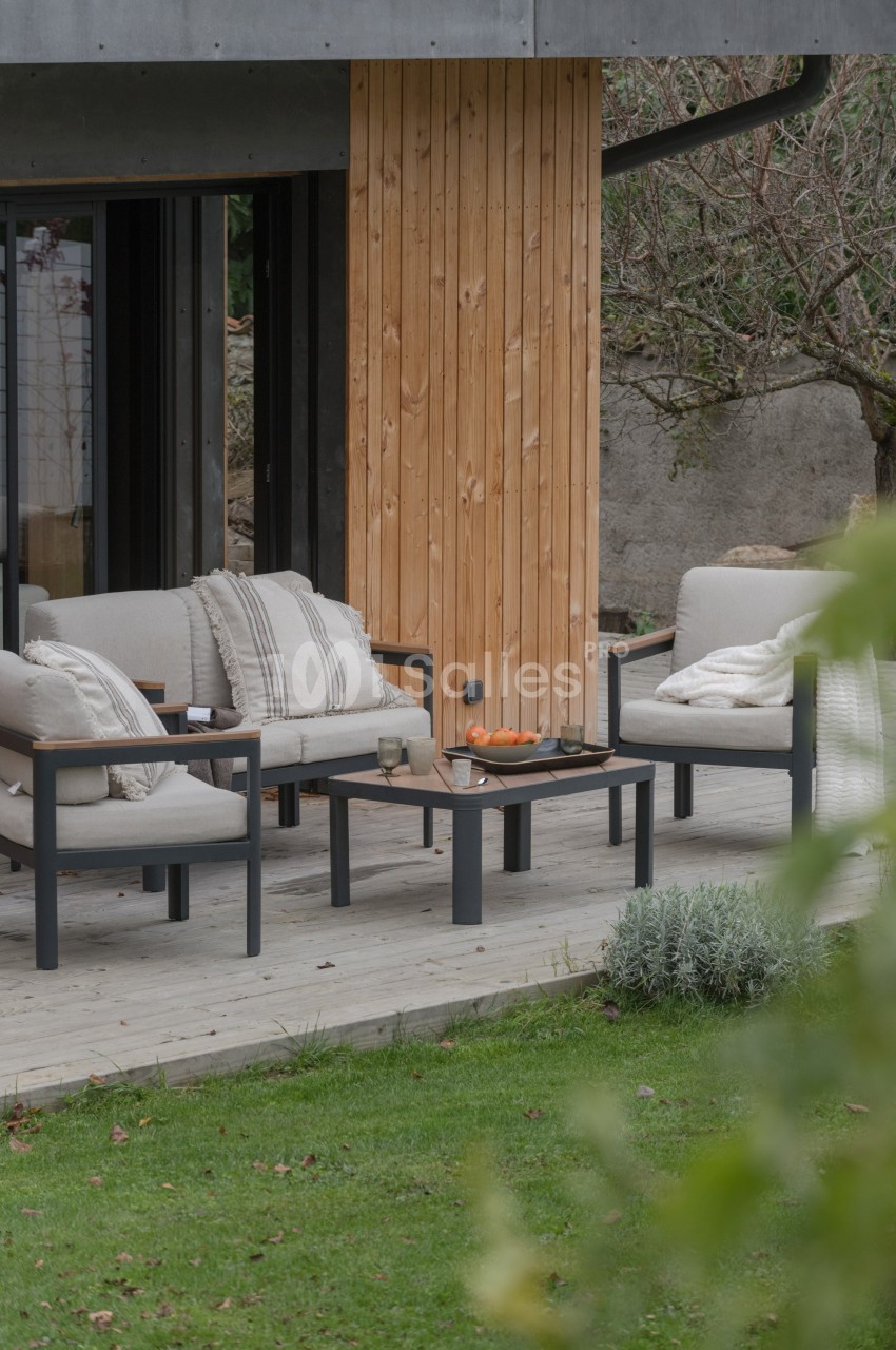 Salon de jardin avec canapés beiges et table basse, installé sur une terrasse en bois près d'un mur en bois clair.