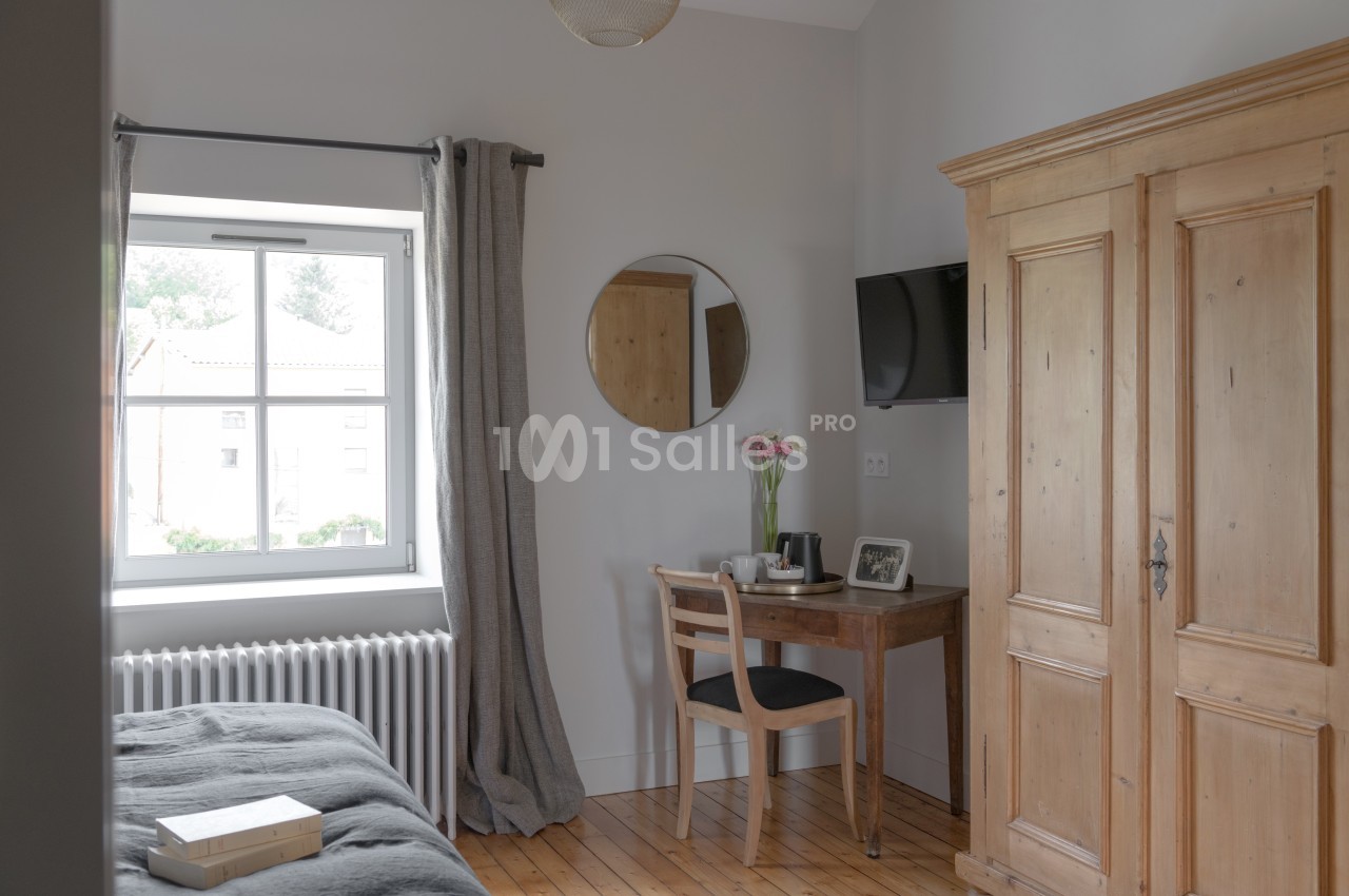 Chambre lumineuse avec un lit, une armoire en bois, un bureau près d'une fenêtre et un miroir rond au mur.