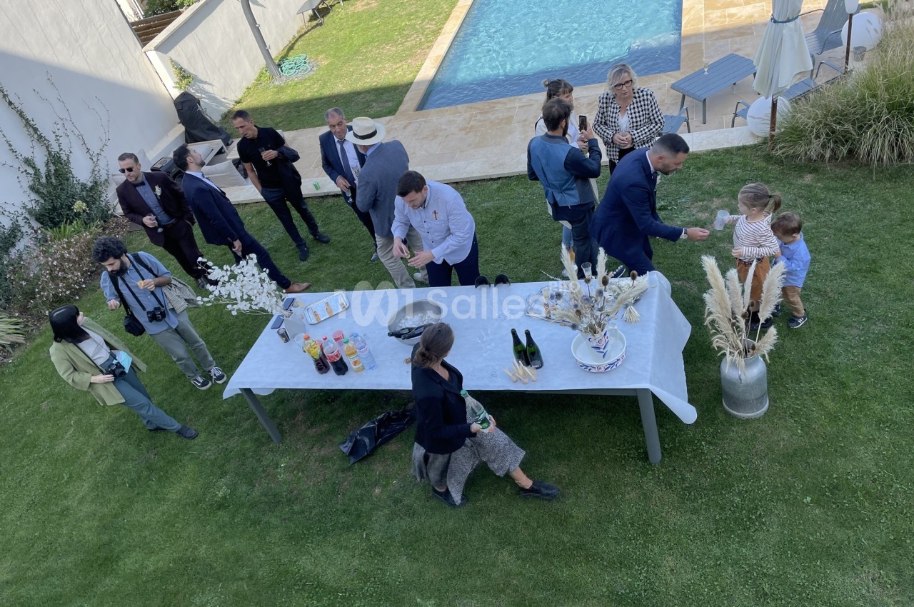 Groupe de personnes réunies autour d'une table en extérieur, près d'une piscine, lors d'un événement convivial.