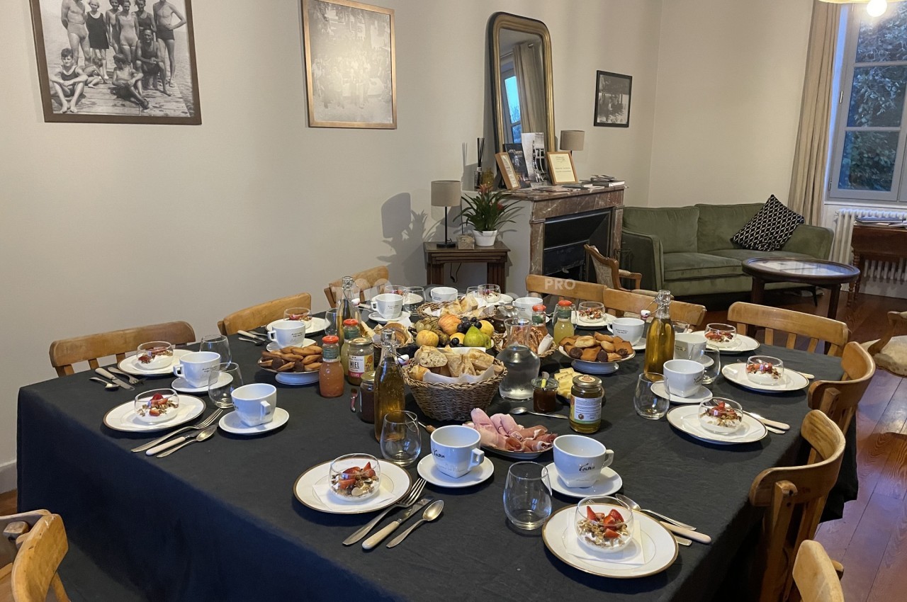 Table dressée pour un repas, avec assiettes, verres, couverts et divers plats, dans une salle à manger chaleureuse.