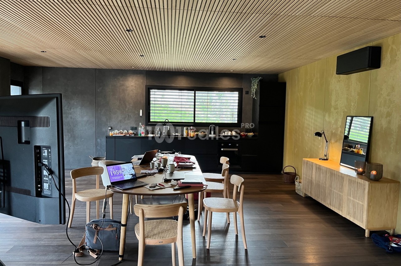 Salle à manger moderne avec table en bois, chaises, cuisine ouverte en arrière-plan et plafond en lambris.