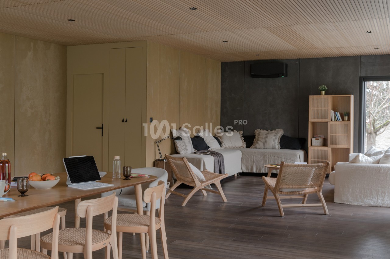 Salon moderne avec mobilier en bois clair, canapé blanc, étagères, table avec ordinateur et grande fenêtre donnant sur l…