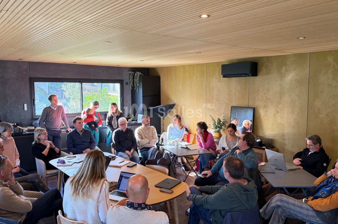 Un groupe de personnes assises autour de tables en réunion dans une salle lumineuse avec un plafond en bois.