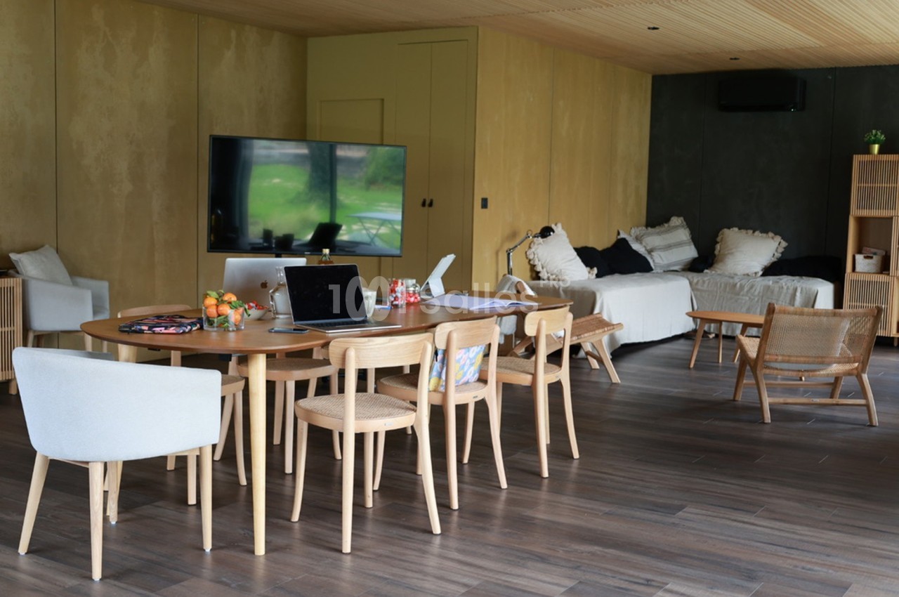 Salle de séjour lumineuse avec table en bois, chaises, canapé, télévision et décoration minimaliste.