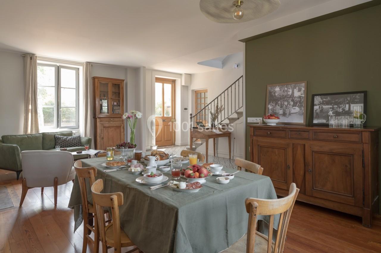 Salle à manger lumineuse avec table dressée pour le petit-déjeuner, meubles en bois et mur vert olive en arrière-plan.