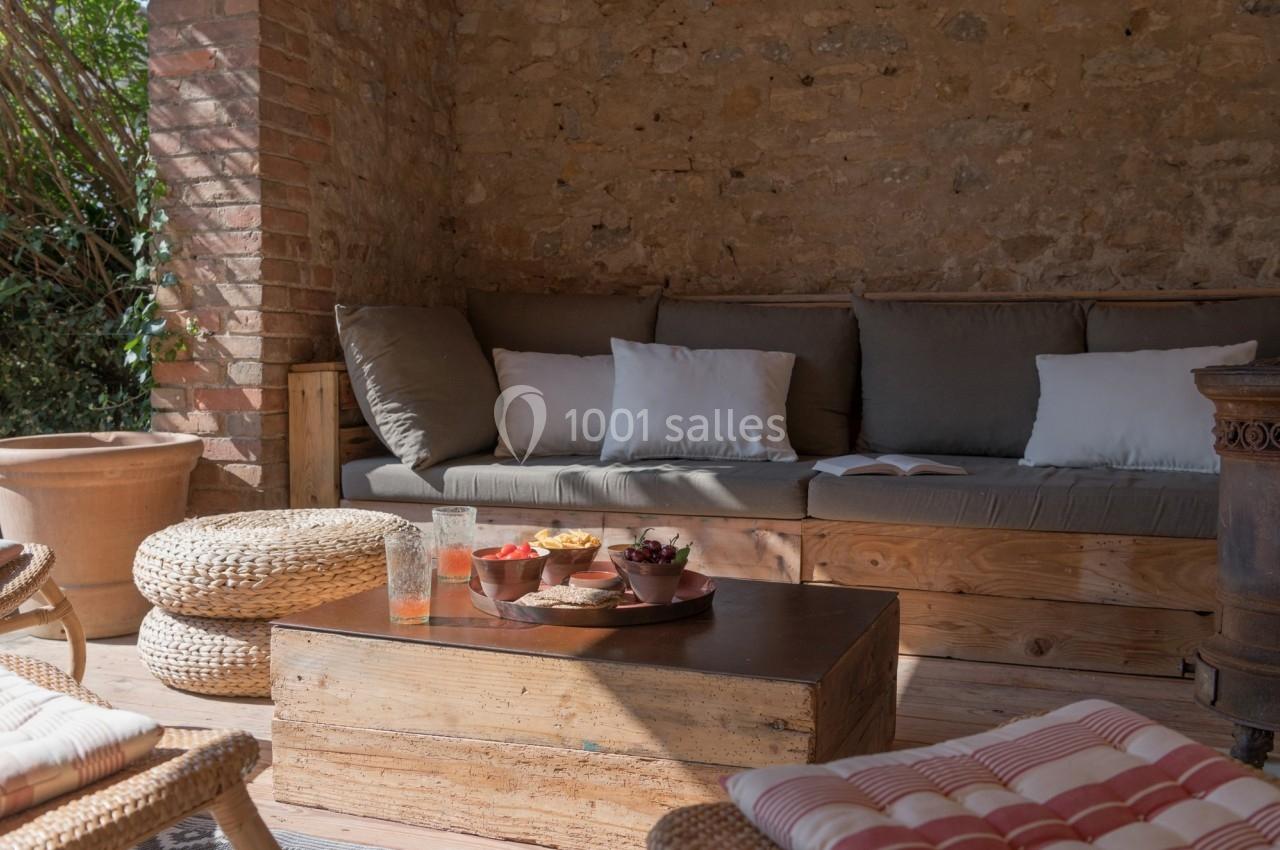 Espace extérieur avec canapé, coussins, table basse en bois et collations, entouré de murs en pierre.