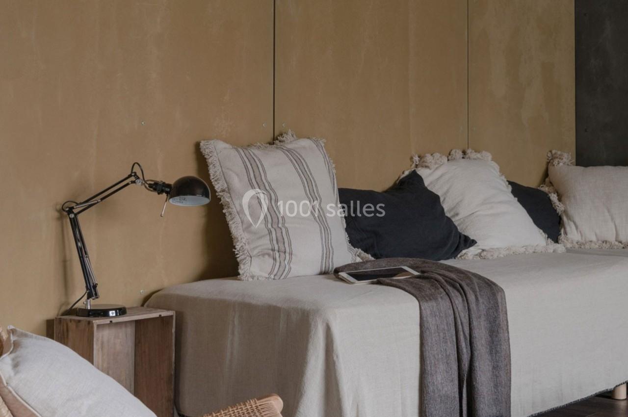 Canapé beige avec coussins blancs et noirs, plaid gris, lampe de bureau noire et table d'appoint en bois.