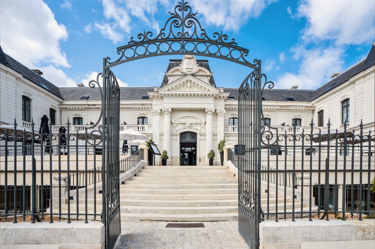 Entrée principale d'un bâtiment historique avec escalier en pierre, portail en fer forgé et façade élégante.